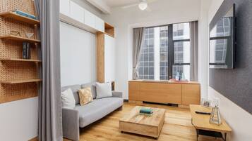 A modern living room with a grey sofa, wooden coffee table, and a wooden shelving unit with books.