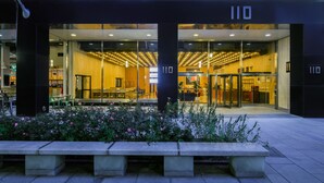 A modern building with a glass facade, a number '110' sign, and a seating area with tables and chairs outside. - Placemakr Wall Street (New York)