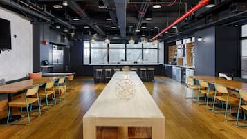 A modern kitchen with a long wooden table and chairs, a central decorative piece, and a view through large windows.