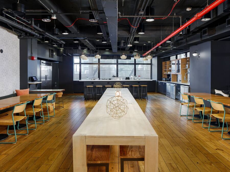 A modern kitchen with a long wooden table and chairs, a central decorative piece, and a view through large windows.