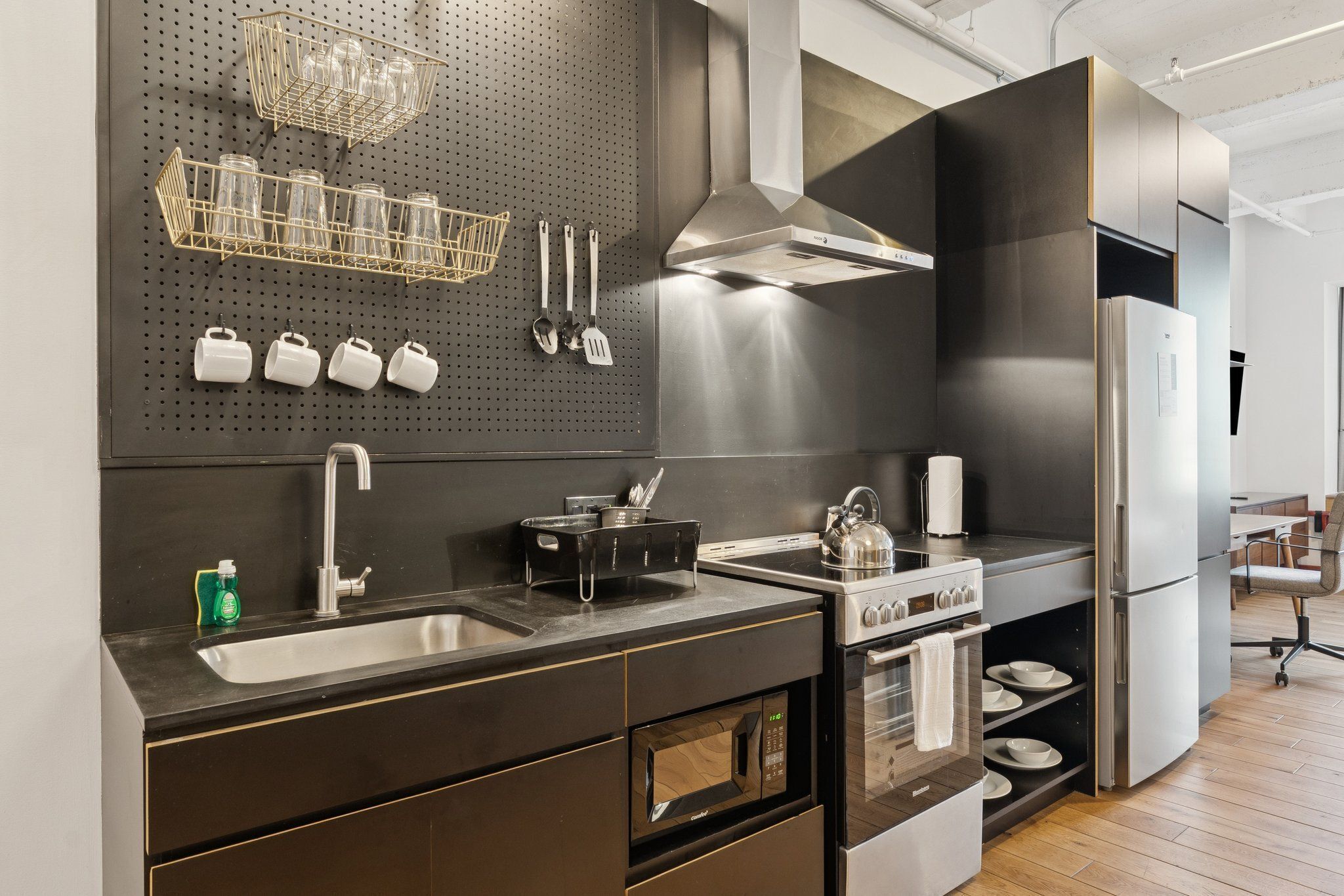 A modern kitchen with stainless steel appliances, a black countertop, and a pegboard with kitchen utensils.