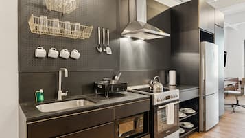 A modern kitchen with stainless steel appliances, a black countertop, and a pegboard with kitchen utensils.