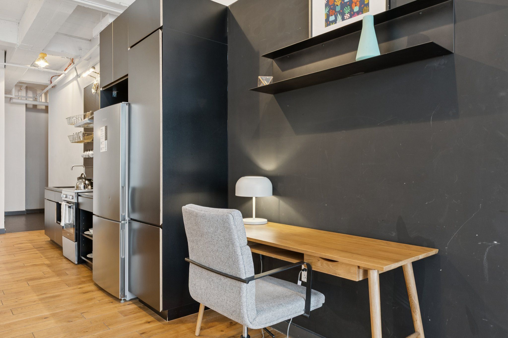 A modern kitchen with a built-in refrigerator, a wooden dining table, and a grey chair.