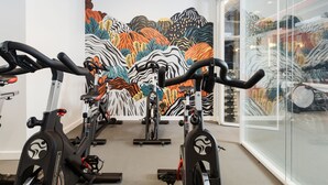 A gym with stationary bikes, a colorful mural on the wall, and a glass wall reflecting the interior. - Placemakr Wall Street (New York)