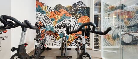 A gym with stationary bikes, a colorful mural on the wall, and a glass wall reflecting the interior.