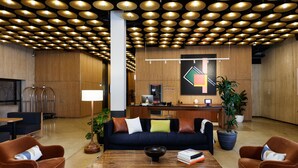 A modern lobby with a wooden reception desk, a black sofa with colorful cushions, and a coffee table with books and a bowl. - Placemakr Wall Street (New York)