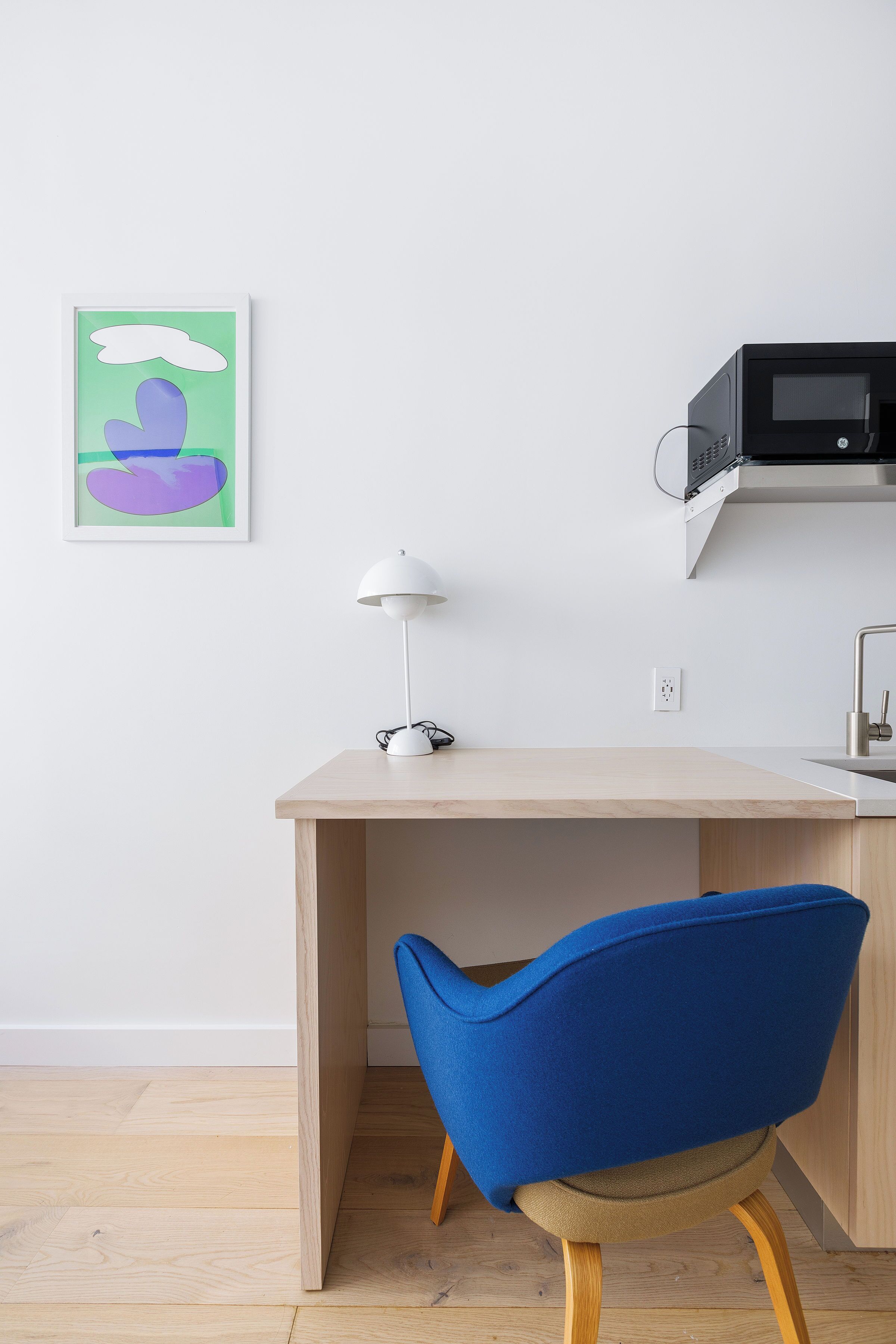 Une cuisine moderne avec un plan de travail en bois, une lampe blanche et une chaise bleue.