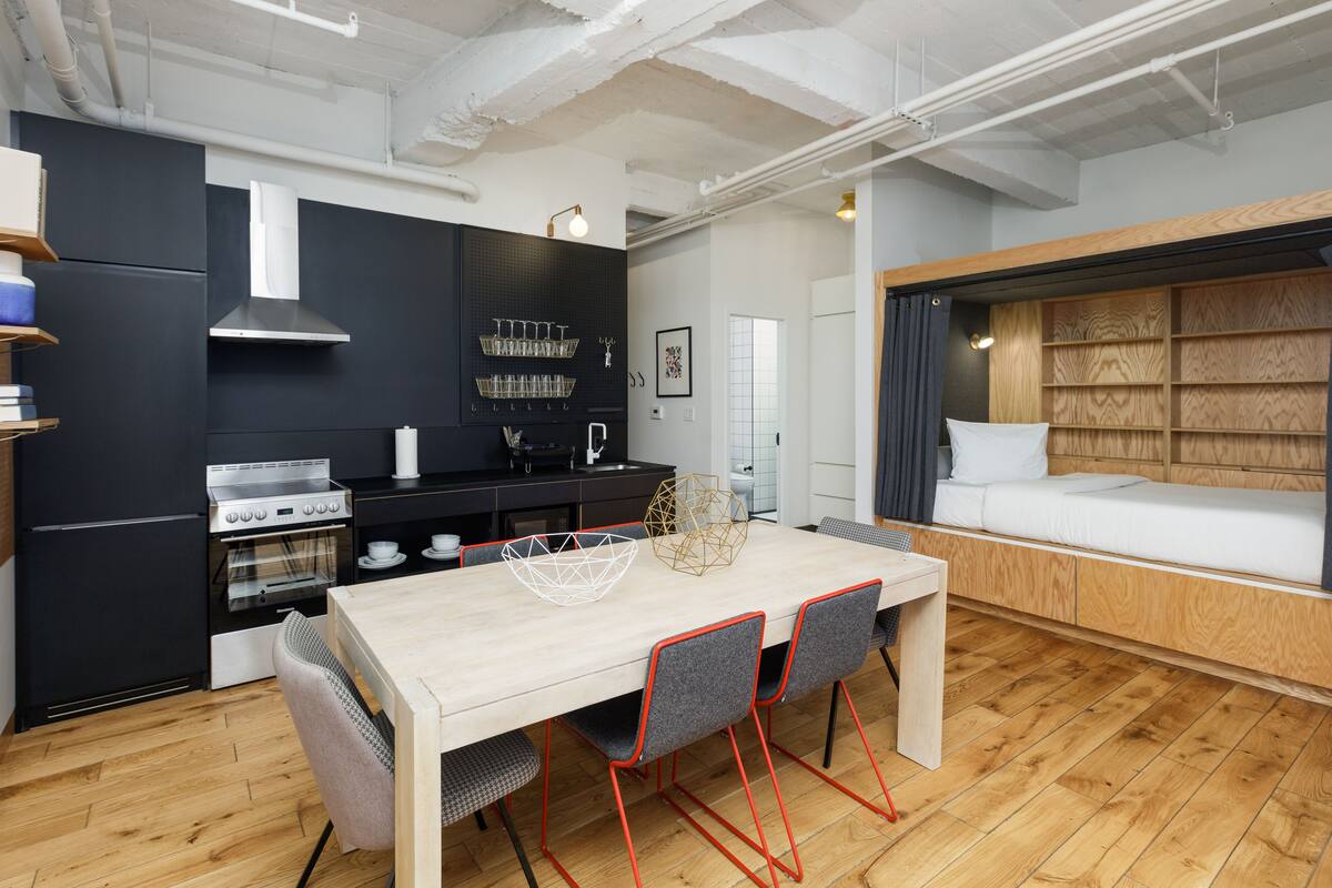A modern kitchen with a dining area, a built-in oven, and a wooden bed with a headboard.