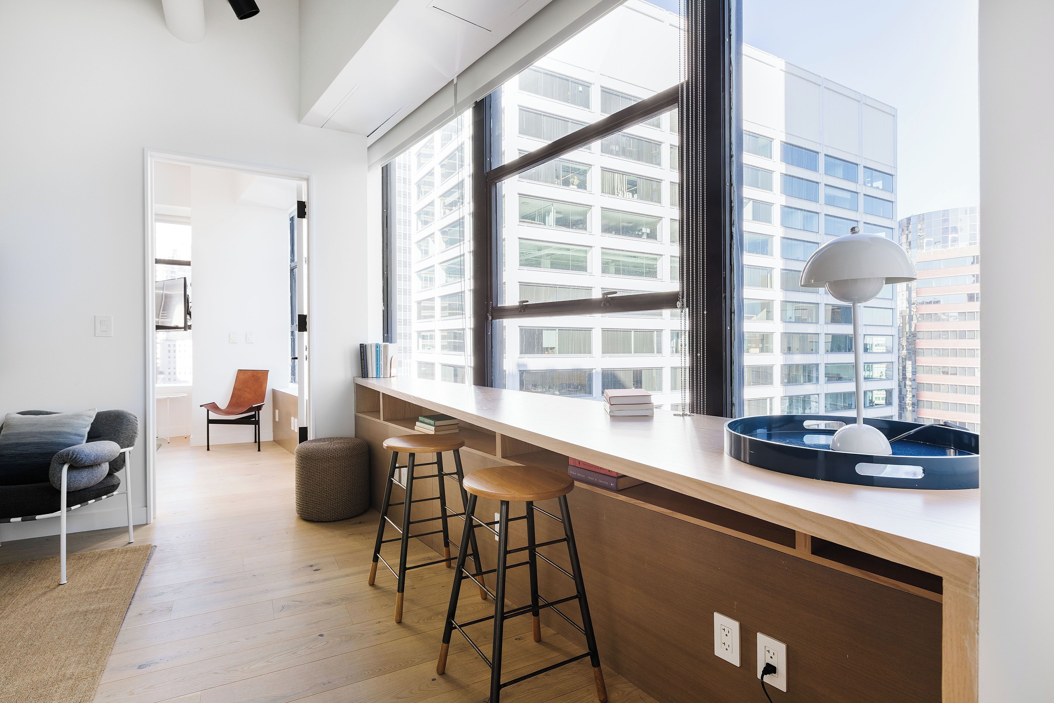 A modern kitchen with a large window, wooden stools, and a bar area.