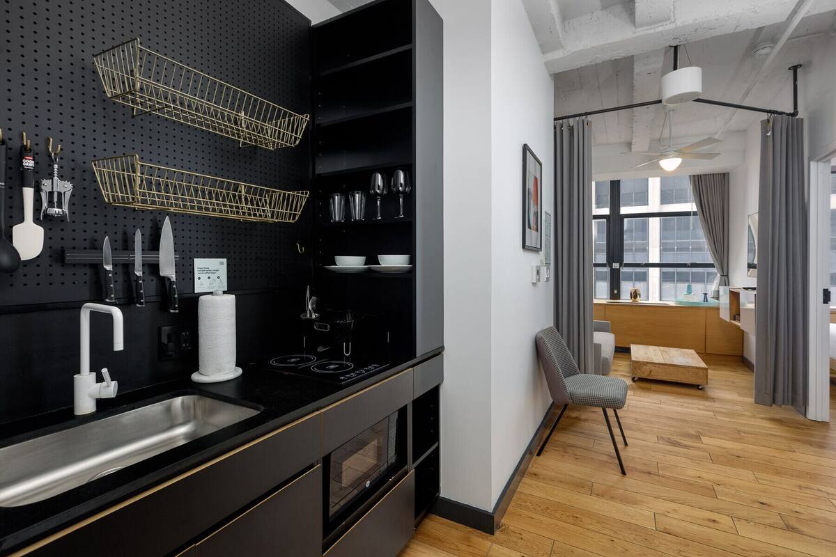 A modern kitchen with a black pegboard wall, stainless steel appliances, and a wooden dining area.