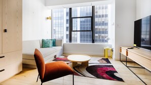 A modern living room with a sofa, a round coffee table, a vibrant rug, and a television. - Placemakr Wall Street (New York)