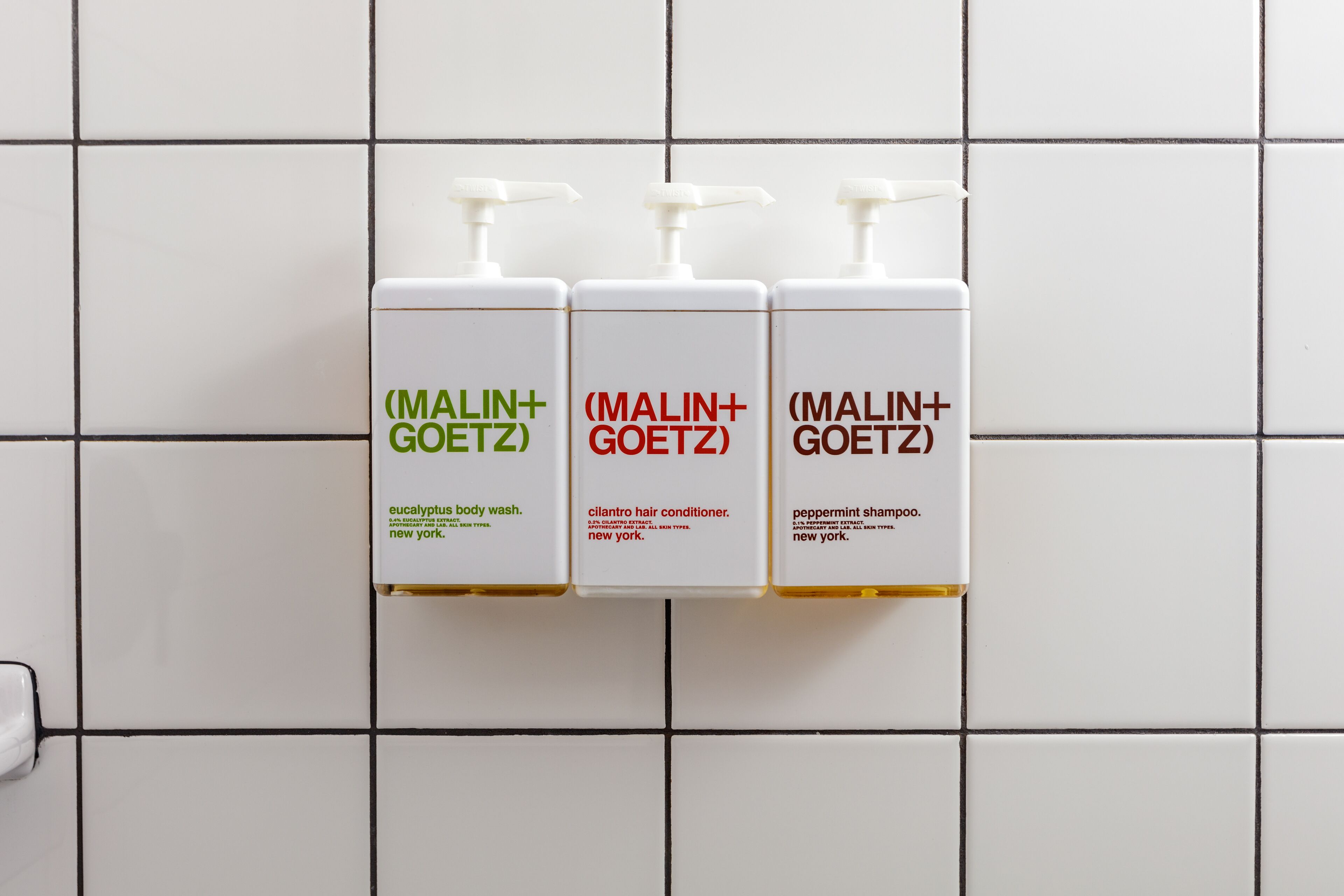 Three white bottles with labels on a tiled wall.