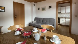 A dining area with a wooden table set for two, a grey sofa, and a kitchen visible through an open doorway. - Jaggler by Interhome (Wildschönau)
