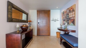 A hallway with a wooden door, a console table with decorative items, a bench, and a wall with abstract art.
