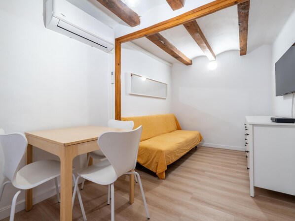 A room with a wooden ceiling, white walls, a bed with a yellow cover, a small white table with chairs, and a TV on a white cabinet. - Apartment in TGN historic center only 450m beach (Tarragona)