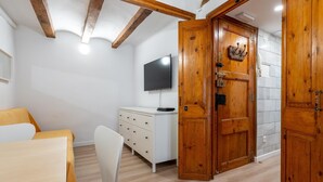 A room with a wooden door, a white dresser, a TV on the wall, and a chair. - Apartment in TGN historic center only 450m beach (Tarragona)