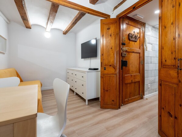A room with a wooden door, a white dresser, a TV on the wall, and a chair.
