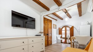 A room with a TV mounted on the wall, a wooden ceiling, a white dresser, a yellow sofa, and a dining area with chairs and a table. - Apartment in TGN historic center only 450m beach (Tarragona)
