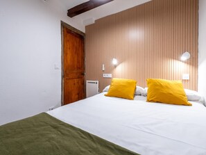 A hotel room with a wooden door, a bed with white bedding and two yellow pillows, and a green throw blanket. - Apartment in TGN historic center only 450m beach (Tarragona)