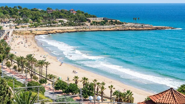 A coastal beach with clear blue waters, sandy shore, and a rocky outcrop. - Apartment in TGN historic center only 450m beach (Tarragona)