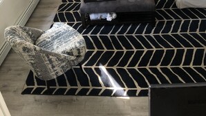 Uma sala de estar com sofá, mesa de centro, tapete estampado e uma poltrona.