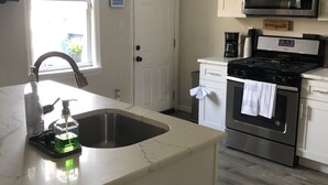 Cozinha com bancada de mármore, pia, fogão de aço inoxidável, micro-ondas e cafeteira.