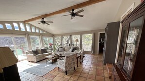 A spacious living room with a high ceiling, large windows, and two ceiling fans.
