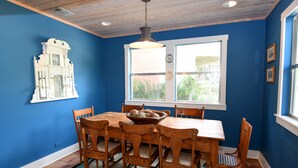 A dining room with a wooden table and chairs, a decorative wall piece, and a window with a view of greenery.