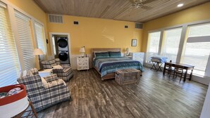 A bedroom with a bed, a desk, a chair, a washing machine, and a laundry basket.