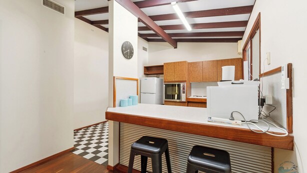 A compact kitchen with a wooden countertop, a built-in microwave, and a refrigerator. There are two stools and a clock on the wall. - The Newby -  Perfect for a couple of families seeking a  getaway together. (Lancelin)