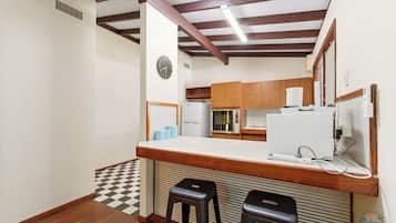 A compact kitchen with a wooden countertop, a built-in microwave, and a refrigerator. There are two stools and a clock on the wall.