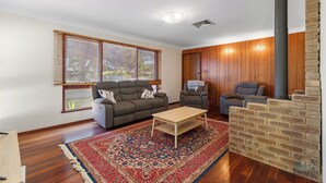 A living room with a sofa, two armchairs, a coffee table, a patterned rug, a brick fireplace, and wooden walls. - The Newby -  Perfect for a couple of families seeking a  getaway together. (Lancelin)