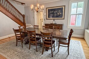 A dining room with a large wooden table surrounded by chairs, a chandelier, and a motivational quote on the wall.