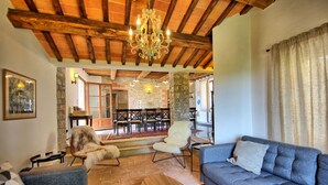 A cozy living room with a wooden ceiling, a chandelier, a blue sofa, and a fluffy chair. - Villa Collina - Holiday House Rental with private swimming pool in the small  village of Montegi... (Montegiove)