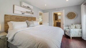 Une chambre dotée d’un grand lit, d’une table de chevet, d’un climatiseur fixé au mur et d’une porte donnant accès à une salle de bain.