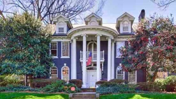 Una casa señorial con fachada simétrica, una entrada central con columnas y una bandera.