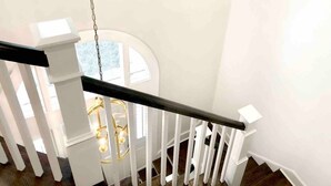 Una escalera blanca con barandilla negra, balaustres blancos y una lámpara colgante.