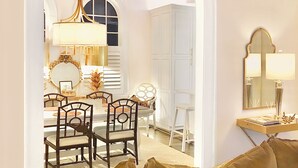 Un comedor con una mesa, sillas y una araña. Se aprecia un armario blanco y un espejo en la pared.