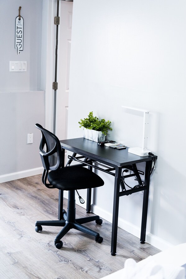 A modern office desk with a chair, a small plant, and a power strip on the floor.