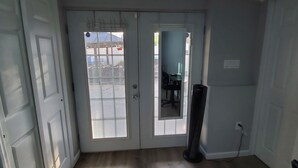 Una habitación con piso de madera, una puerta blanca y vista a un espacio exterior por una puerta de cristal.