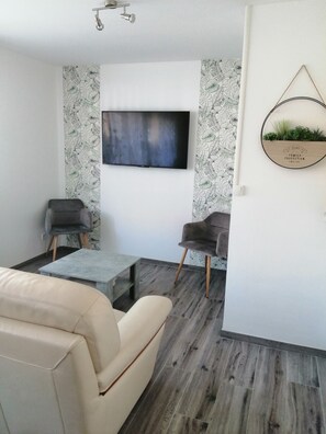 A modern living room with a beige sofa, two armchairs, a coffee table, and a flat-screen TV mounted on the wall. - Gîte baie de somme (Friville-Escarbotin)