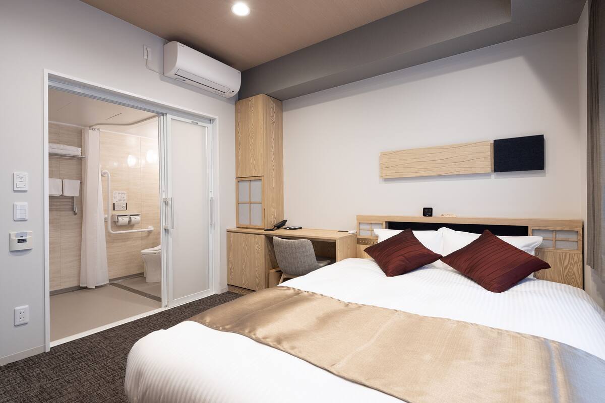 Een hotelkamer met een bed, een bureau, een stoel, een douche en een wandgemonteerde televisie.
