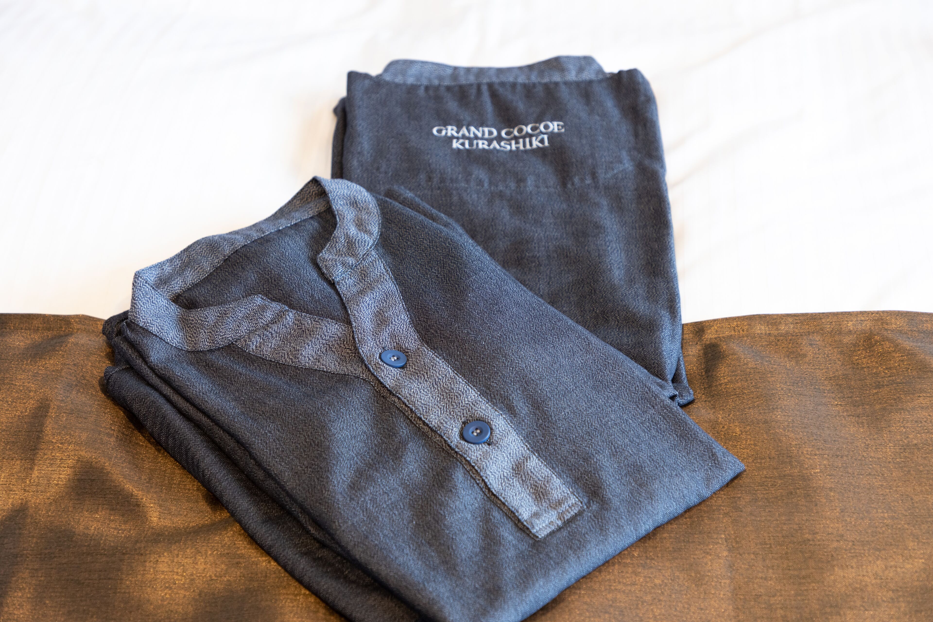 A neatly folded dark blue shirt with a collar and buttons, and a matching dark blue t-shirt with text on it, both placed on a wooden surface.