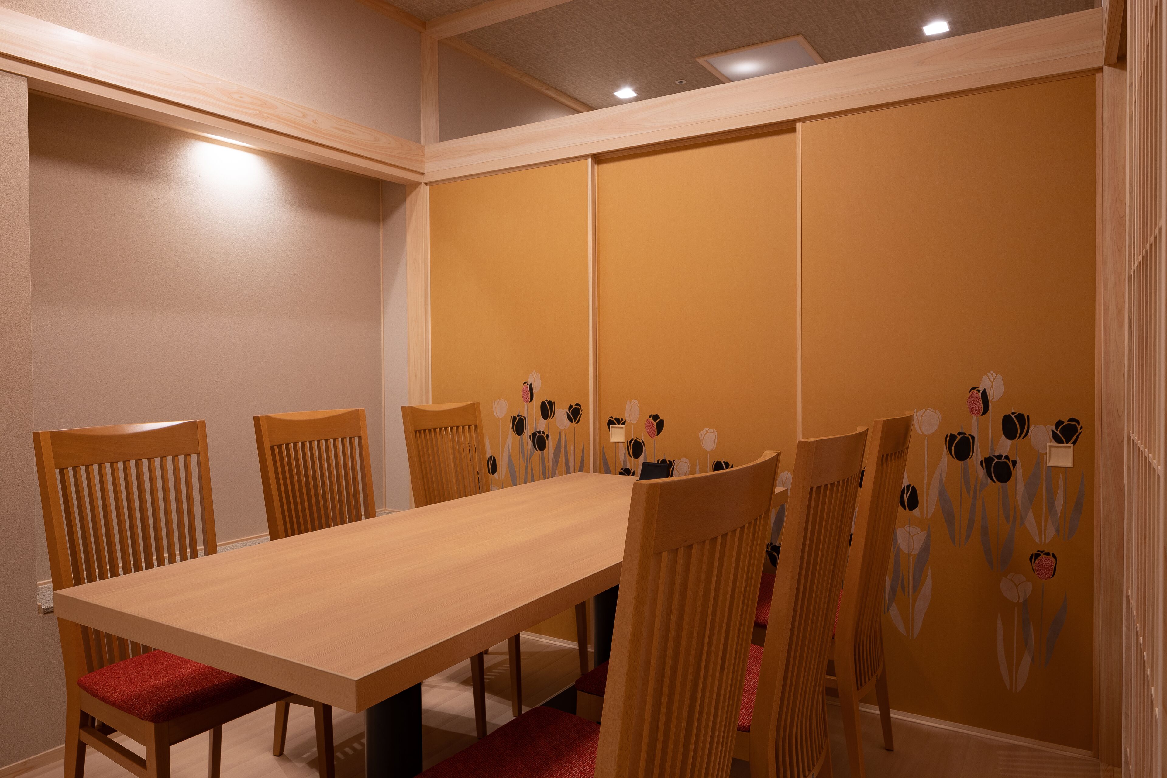A conference room with a long table and six wooden chairs with red cushions.