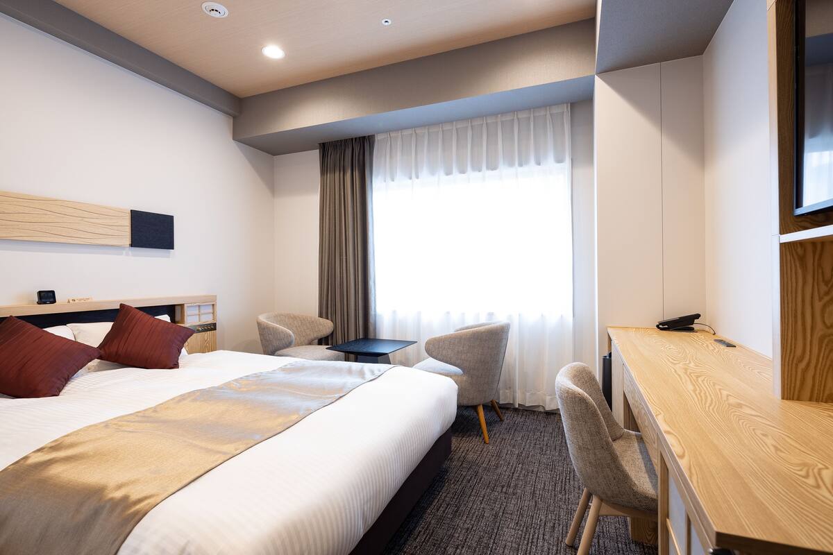 Een hotelkamer met een bed, een bureau, een stoel, een televisie en een raam met gordijnen.