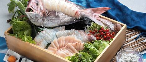 Una caja de madera con diversos productos del mar, como pescado y mariscos, junto con recipientes pequeños de salsas.