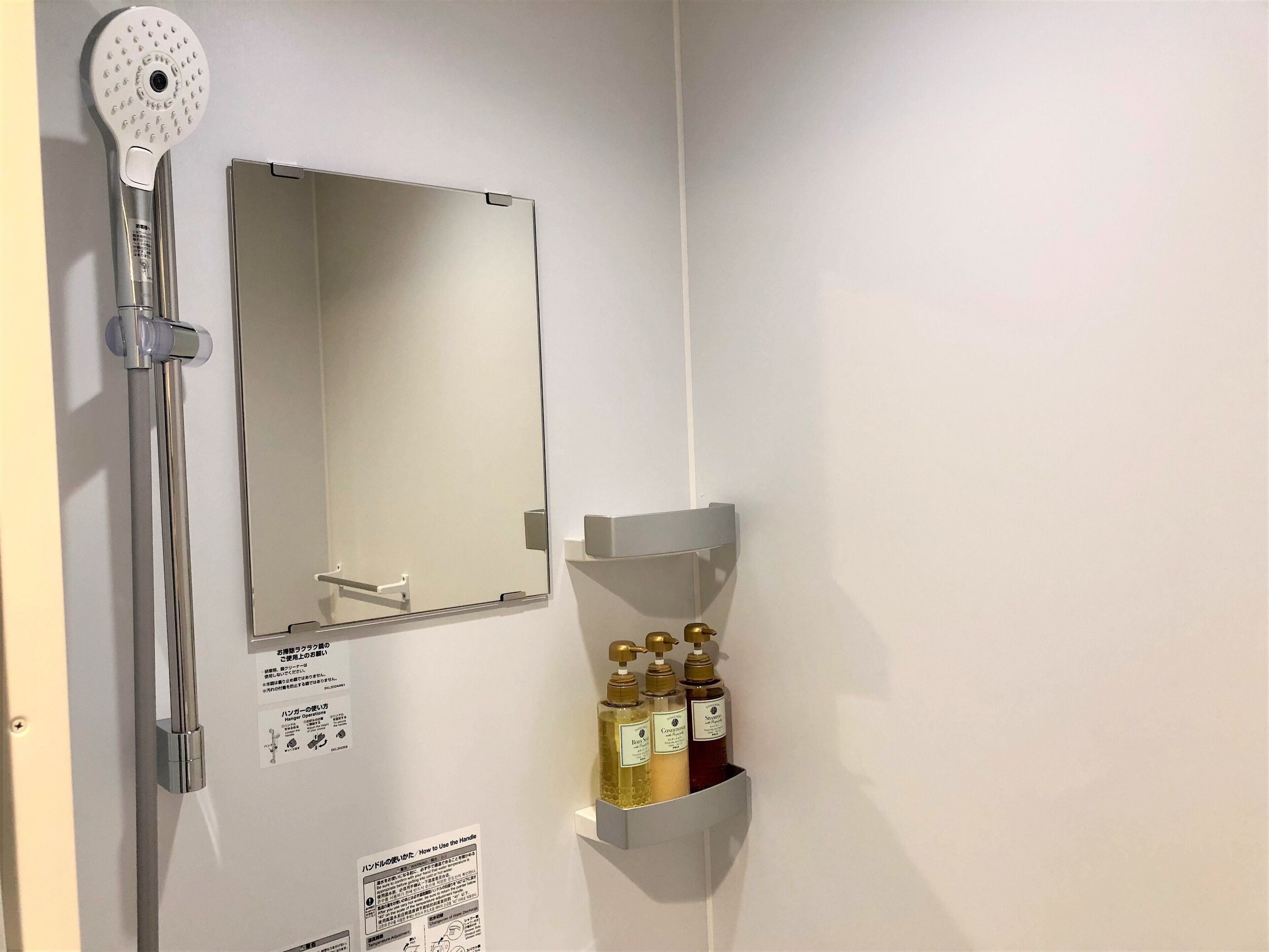 A bathroom with a shower, a mirror, and a shelf with toiletries.
