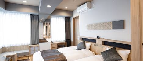 A hotel room with two beds, a desk, and a window with curtains.