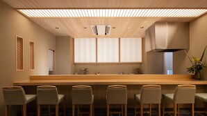 Un bar moderno con taburetes de madera, una barra alargada e iluminación empotrada en el techo.