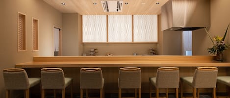 Un espace bar moderne avec des tabourets en bois, un long comptoir et un plafond doté d’un éclairage encastré.